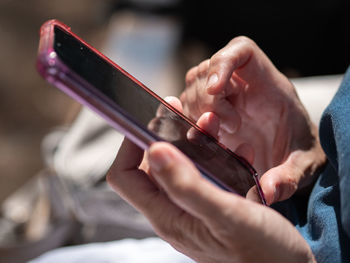 Detail of the hands of a woman using her mobile phone with pink cover.