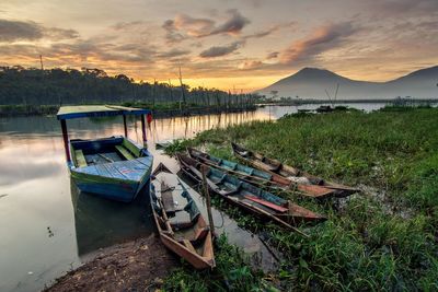 Boats moored on lake against sky during sunset