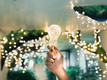 Cropped hand of woman holding illuminated light bulb