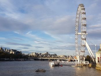 Bridge over river in city against cloudy sky