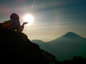 Silhouette man lying on mountain against sky during sunset