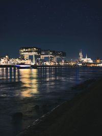 Illuminated buildings by sea against sky at night