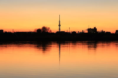 Silhouette buildings by lake against sky during sunset