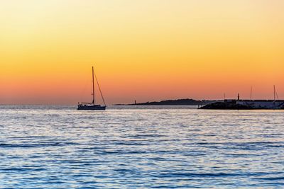 Sailboat sailing on sea against orange sky