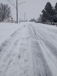 Road by snow covered trees against sky