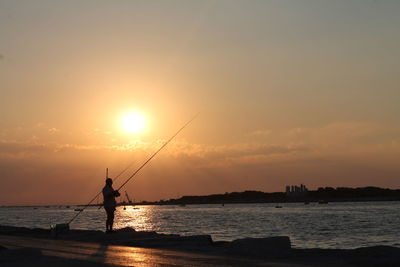 Silhouette man fishing in sea against sky during sunset