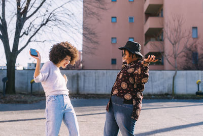 Cheerful friends with mobile phone dancing on road