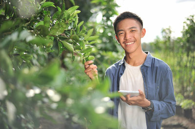 Happy of smiling young asian farmer male holding the notebook on green garden