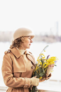 A young woman in a beige coat and hat with a bouquet of mimosa. international women's day