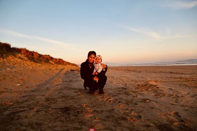 Full length of woman with son on beach against sky during sunset