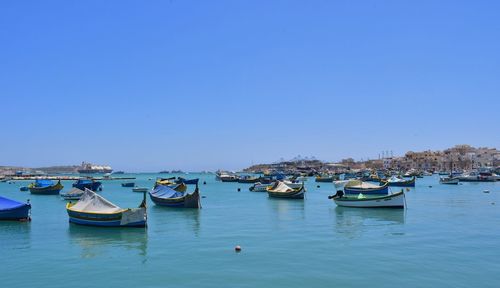 Boats moored in harbor against clear blue sky