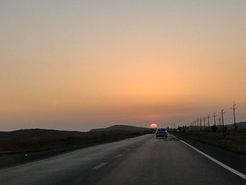 Cars on road against clear sky at sunset