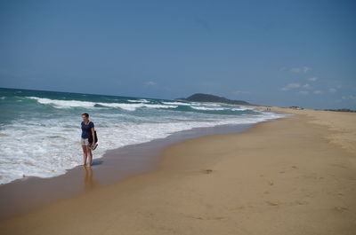 Rear view of man walking on beach against clear sky