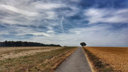 Empty road amidst agricultural field against sky