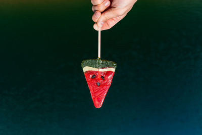 Close-up of hand holding lollipop against colored background