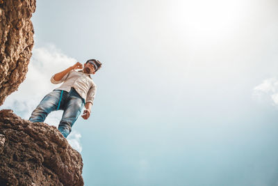 Low angle view of man standing on rock against sky