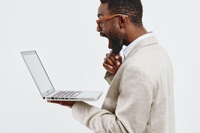 Side view of man using laptop while standing against white background