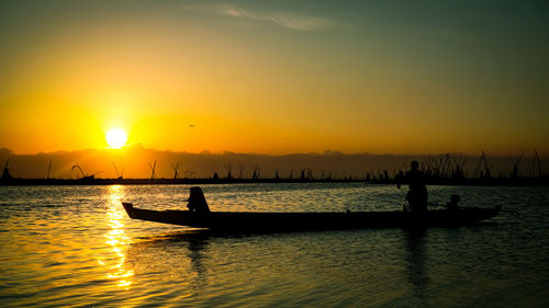 Silhouette people on boat in sea against sky during sunset