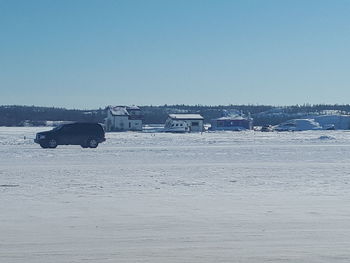 Car on snow covered landscape against clear blue sky