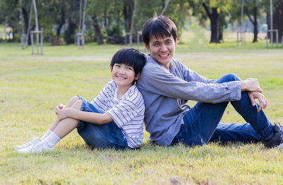 View of father and son sitting on grass in park