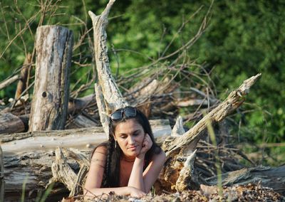 Portrait of smiling young woman lying on log in forest