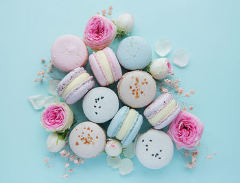 Tasty macaroons with beautiful roses on a blue background