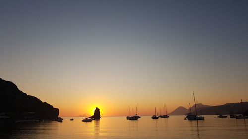 Silhouette sailboats in sea against clear sky during sunset