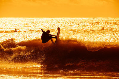 Silhouette person in sea against sky during sunset