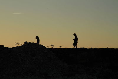 Silhouette men standing on land against clear sky during sunset