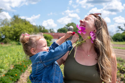 Smiling mother and daughter standing on field against sky