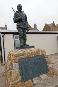 Statue of man standing by building against sky