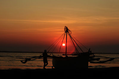 Silhouette of fishing boat in sea against sunset sky