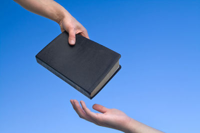 Close-up of hands with bible against blue background