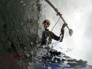 Low angle view of man kayaking on sea against cloudy sky