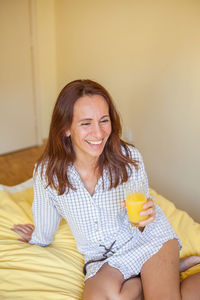 Cheerful woman having drink on bed at home