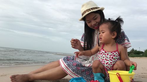 Smiling mother sitting with baby girl playing on shore at beach