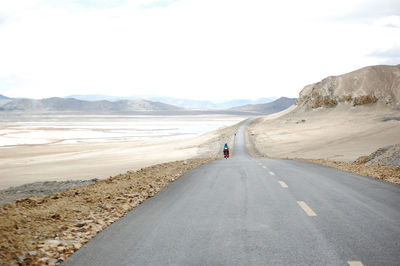 Rear view of man walking on road against sky