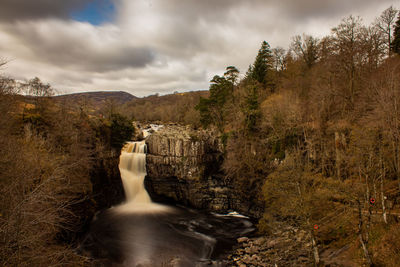 Scenic view of waterfall amidst trees against sky