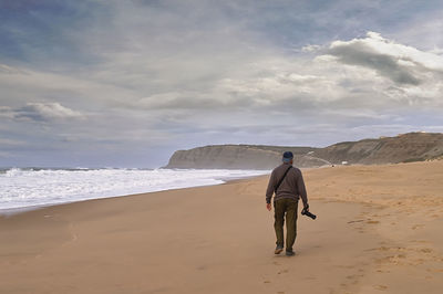 Rear view of man walking at beach against sky