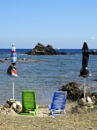 Empty lounge chairs and closed parasols at beach against clear sky