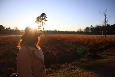 Woman standing on field against sky during sunset