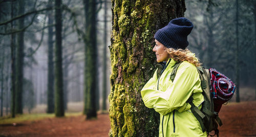 Woman standing by tree trunk in forest