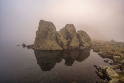 Rock formation in water against sky