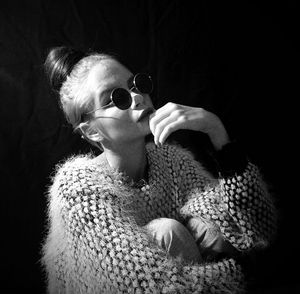 Fashionable woman wearing sweater and sunglasses against black background