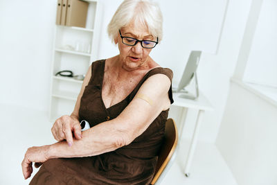 Senior woman with bandage on arm sitting at hospital