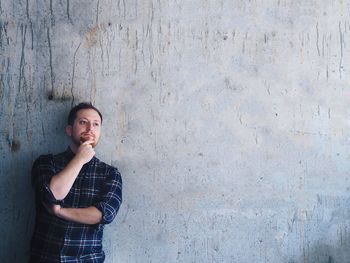 Thoughtful young man with hand on chin against wall