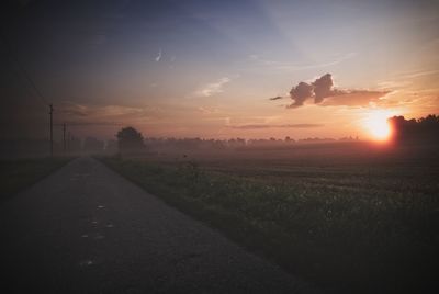 Road amidst field against sky during sunset