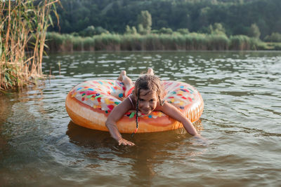 Girl has fun on big donut inflatable ring on lake on hot summer day, happy summertime, countryside