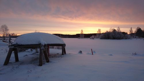 Snow covered field against sky during sunset