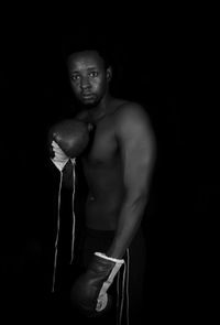 Portrait of shirtless man standing against black background